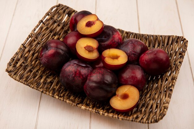 Top view of juicy and sweet pluots on a wicker tray on a beige wooden wall