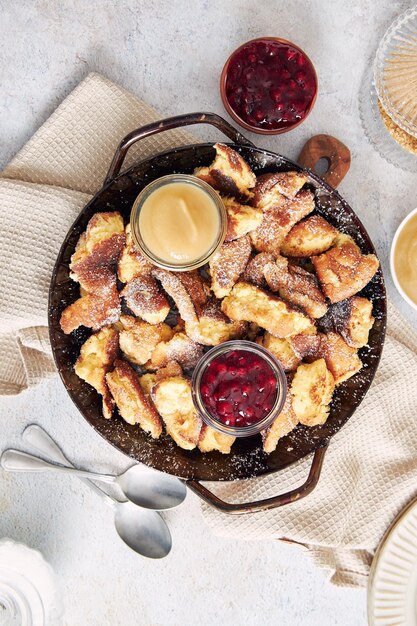 Top view of kaiserschmarrn with torn pancakes, cranberries jam, and apple puree on a table