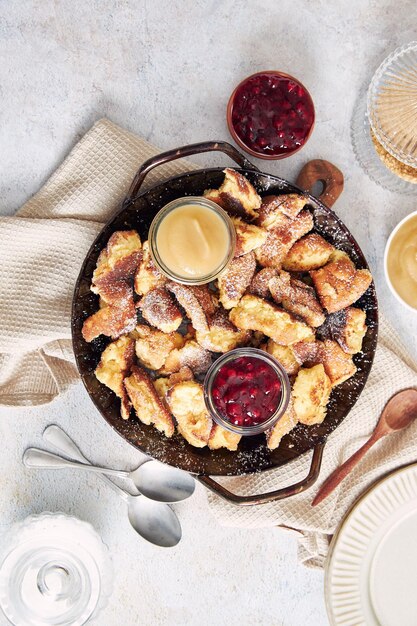 Top view of kaiserschmarrn with torn pancakes, cranberries jam, and apple puree on a table