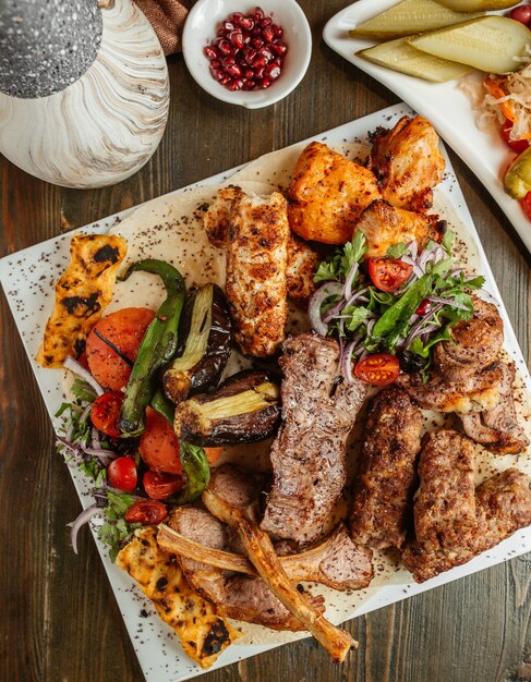Верхний вид на тарелку с ребрами, курицей, лулой, тиккой и овощами.