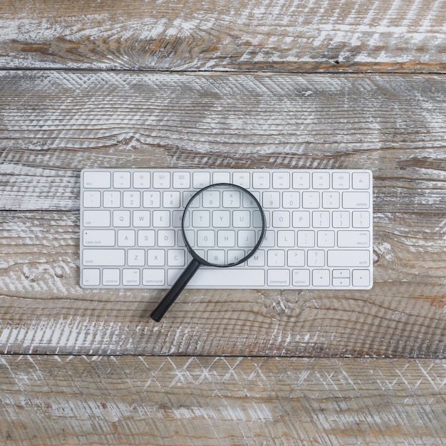 Top view keyboard with magnifier on wooden background. vertical