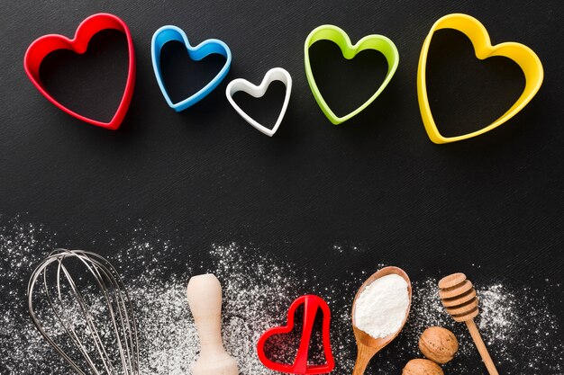 Top view of kitchen utensils with colorful heart shapes and flour