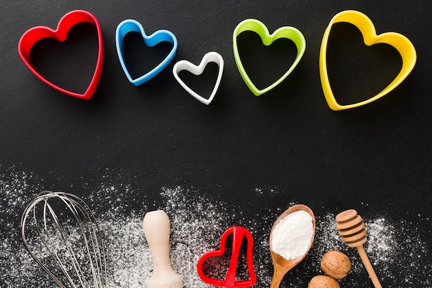 Top view of kitchen utensils with colorful heart shapes and flour