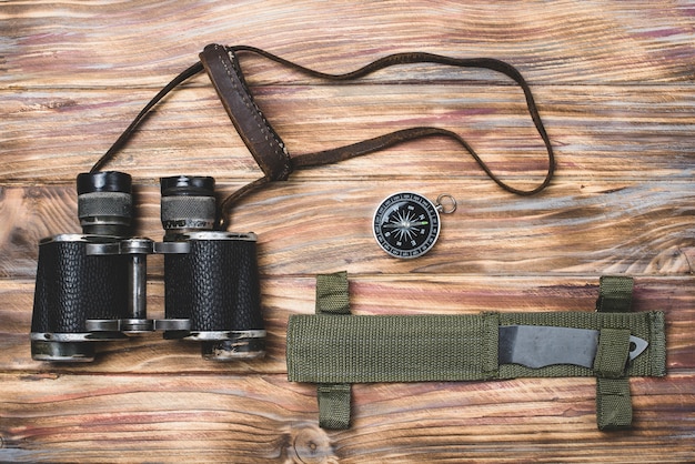 Top view of knife, compass and binoculars on wooden surface