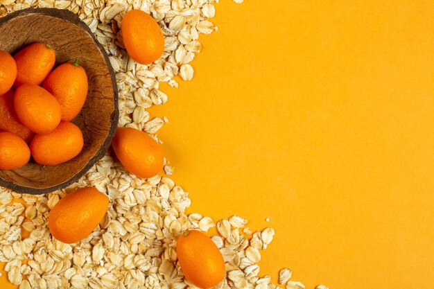 Top view of kumquat in a wooden bowl and oat flakes with copy space on yellow