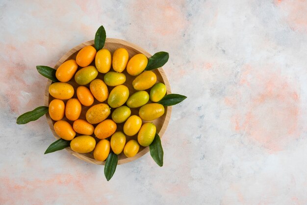 Top view of kumquats and leaves on wooden plate