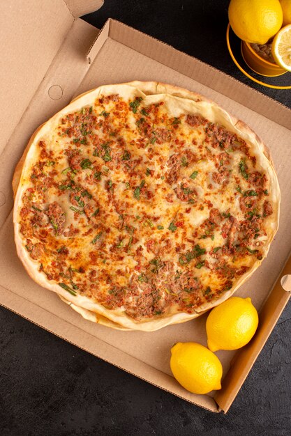 A top view lahmacun dough with minced meat along with greens and lemon inside paper box tasty pastry meal