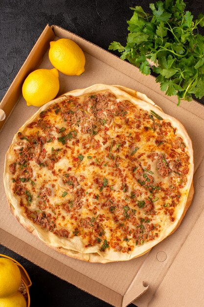 A top view lahmacun dough with minced meat with greenies and lemon inside paper box tasty pastry meal