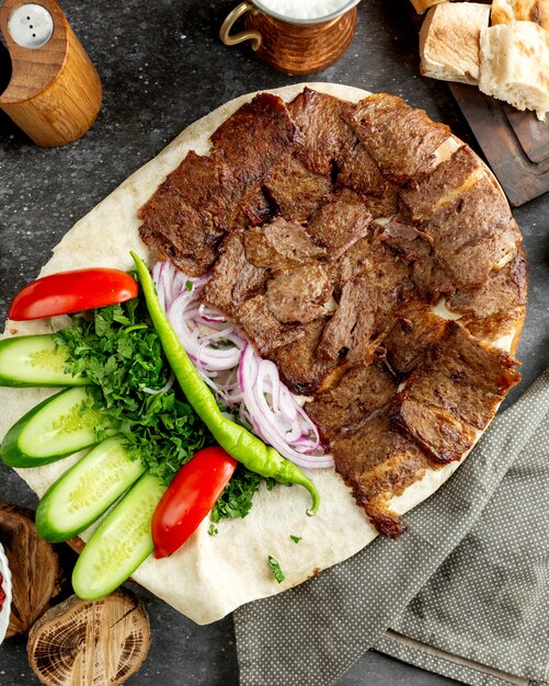 Top view of lamb doner slices placed on flatbread with green salad and onions