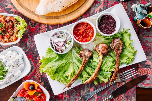 Top view lamb ribs kebab on salad leaves with sauces and onions