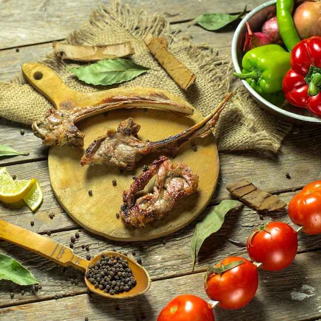 Top view of lamb ribs kebab served with fresh vegetables on a wooden cutting board