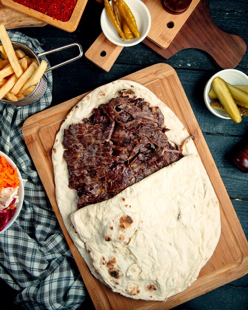Top view of lamb steak doner in flatbread served with fries and pickled cucumber