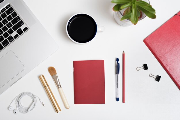 Top view of laptop; coffee cup; earphone; and pen; make-up brush; mascara; potted plant on white background