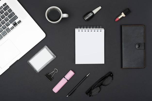 커피 컵 노트북의 상위 뷰; 립스틱; 검은 배경에 네일 광택 및 사무실 물건