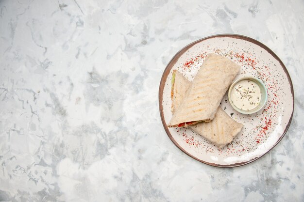 Top view of lavash wrap and yogurt in a small bowl on a plate on the left side on stained white surface