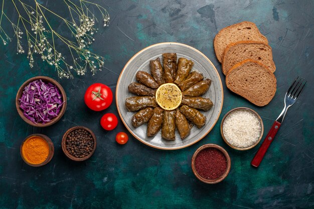 Top view leaf dolma delicious eastern meat meal rolled inside green leaves with tomatoes and bread on blue desk meat food dinner dish vegetable health