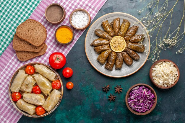 Вид сверху листовой долмы восточное мясное блюдо, завернутое в зеленые листья с хлебом и капустной долмой на темно-синем столе мясное обеденное блюдо восточная еда