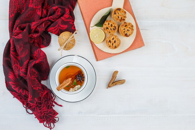 Top view lemon,chocolate chip cookies in plate with red scarf,white cookies,cinnamon and a book on white surface