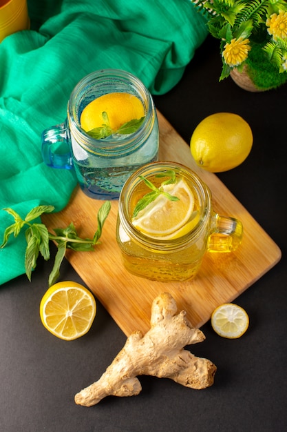 Una bevanda fresca fresca del cocktail del limone di vista superiore dentro le tazze di vetro affettate e limoni interi con i fiori sui precedenti scuri bevono la frutta del cocktail