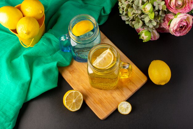 暗い背景のカクテルドリンクフルーツの花と一緒にスライスされたガラスのコップとレモン全体の上面図レモンカクテル新鮮な冷たい飲み物