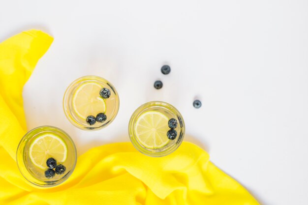 Top view of lemon juice glasses with yellow fabric on white background