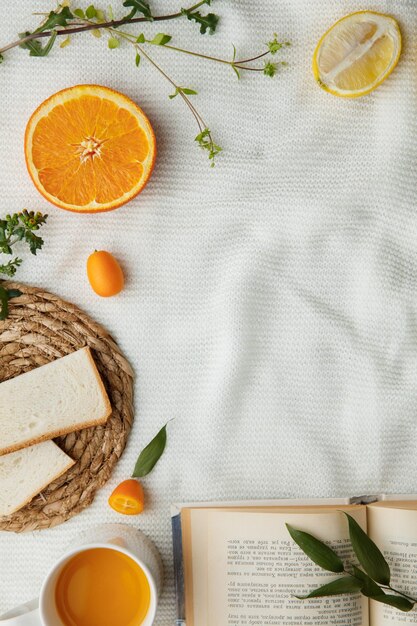 Top view of lemon orange bread slices on trivet and kumquats orange juice with open book on white cloth background