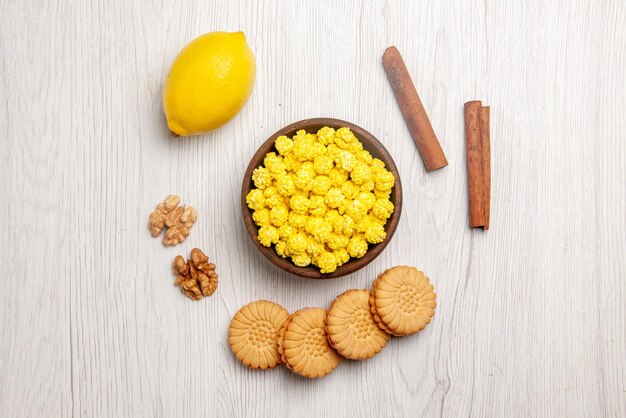 Вид сверху лимон и сладости палочки корицы печенье орехи миска желтых конфет и лимона на белом столе