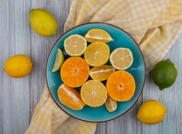 회색 배경에 노란색 체크 무늬 수건에 접시에 라임과 오렌지와 상위 뷰 레몬 웨지