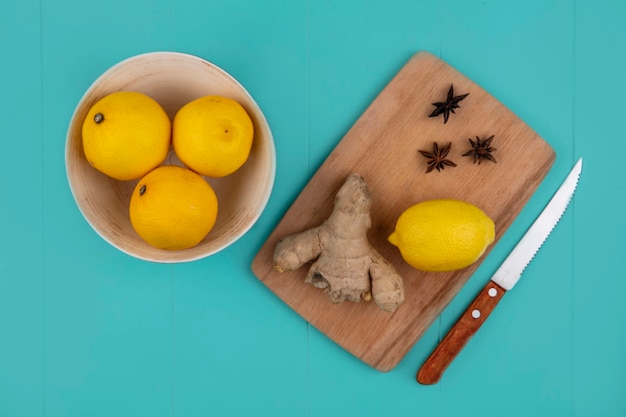 Top view of lemon with ginger on cutting board and knife with bowl of lemons on blue background