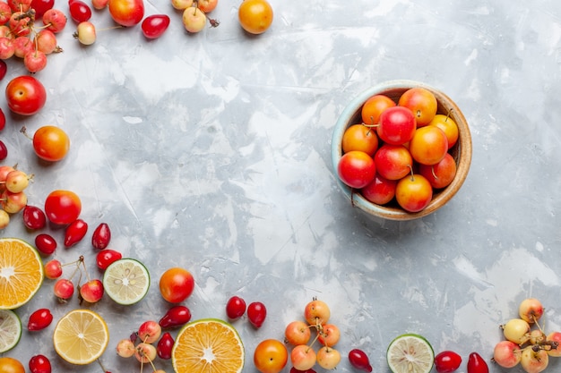 Top view lemons and cherries fresh fruits with pot of cherry-plums on the light desk fruit fresh mellow ripe