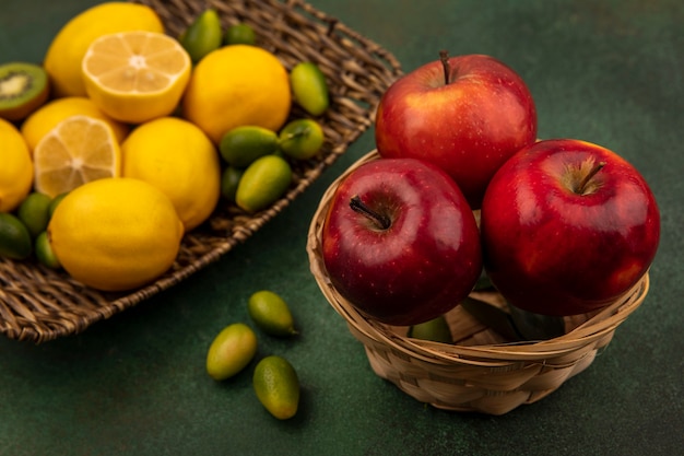 緑の壁のバケツに赤い甘いリンゴとキンカンと籐のトレイにレモンの上面図