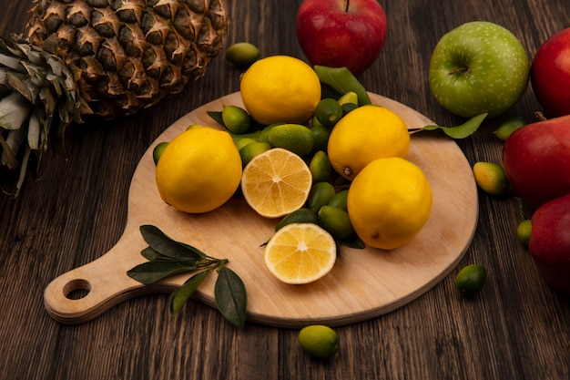 Vista dall'alto di limoni con kinkan isolato su una tavola da cucina in legno con mele e ananas isolato su una parete in legno