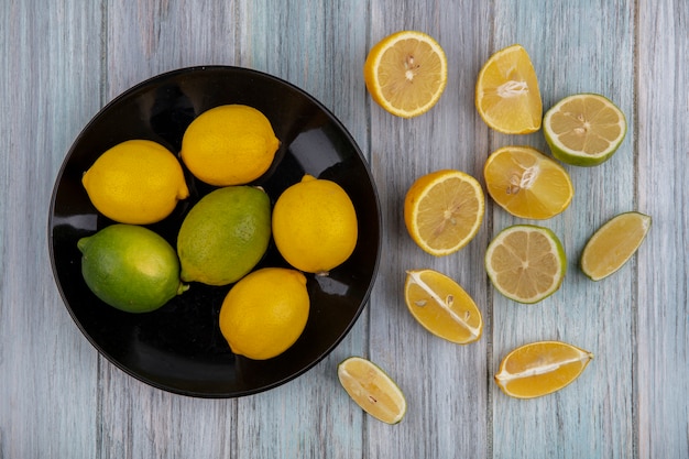 Foto gratuita limoni vista dall'alto con lime su un piatto nero con spicchi su uno sfondo grigio