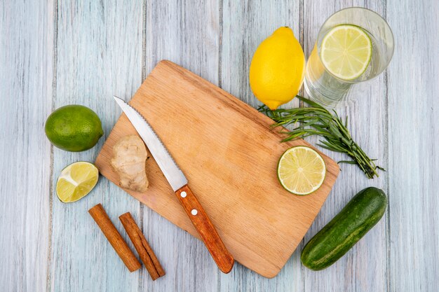 Top view of lemons on a wooden kitchen board with knife with ginger cinnamon sticks and tarragon greens on grey wooden surface