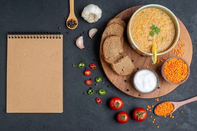 Top view lentil soup with salt raw lentils and dark bread loaves on dark surface