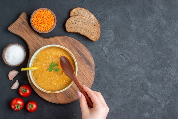 Чечевичный суп с солеными помидорами и темными буханками хлеба на темной поверхности, вид сверху