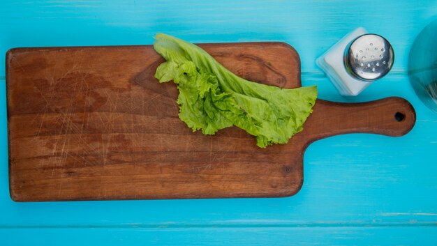 Top view of lettuce on cutting board with salt on blue surface