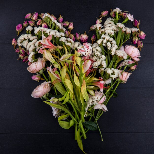 Top view of light pink flowers in the shape of a heart on a black surface