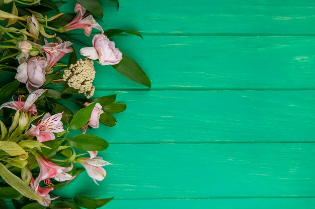 Top view of light pink flowers with leaf branches on a green surface