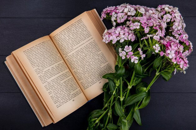 Top view of light pink flowers with an open book on a black surface