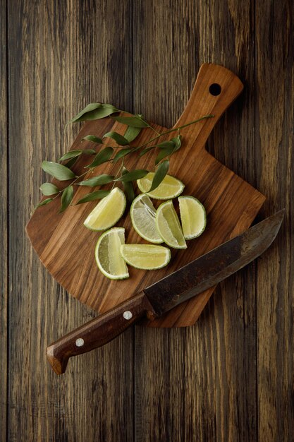 Top view of lime slices with leaves and knife on cutting board on wooden background