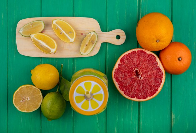 Top view lime slices with lemons on a cutting board with oranges and half a grapefruit on a green background