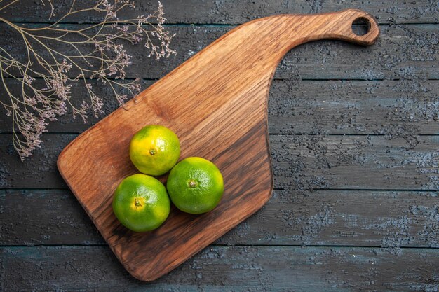 Top view limes on board three limes on cutting board on the table next to the branches