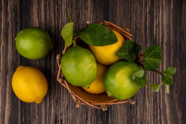 Top view limes with lemons in basket on wooden background