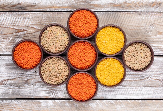 Top view lined up different lentils in brown bowls on beige wooden table. horizontal