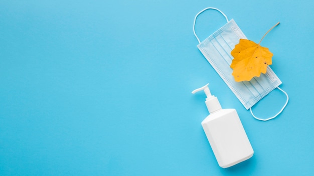 Top view of liquid soap bottle with medical mask and autumn leaf