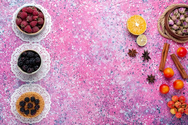 Top view of little blackberry cake with raspberries and fresh blackberries on light pink surface