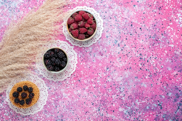 Top view of little blackberry cake with raspberries and fresh blackberries on the light pink surface