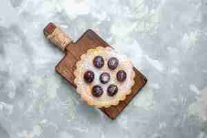 Foto gratuita vista dall'alto di una piccola torta di zucchero a velo con ciliegie sulla scrivania leggera, torta di biscotti al caffè dolce