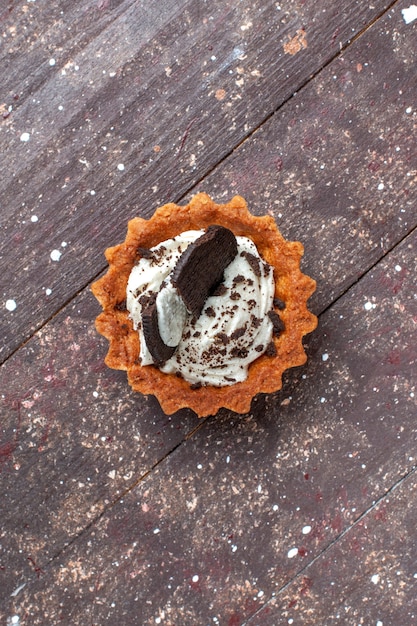 木製の茶色、ケーキビスケットの甘い焼きで分離されたクリームとチョコレートと小さなケーキの上面図